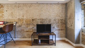 A room with a brick wall, a TV on a wooden stand, a chair, and a table.