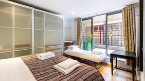 A modern hotel room with a large bed, a massage table, a small table, and a view of the city through large windows. - The Spaceworks Stylish Flat Near Shoreditch (London)