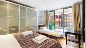 A modern hotel room with a large bed, a small sofa, a desk, and a sliding glass door to the outside.