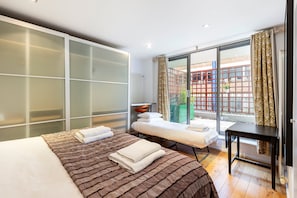 A modern hotel room with a large bed, a small sofa, a desk, and a sliding glass door to the outside.