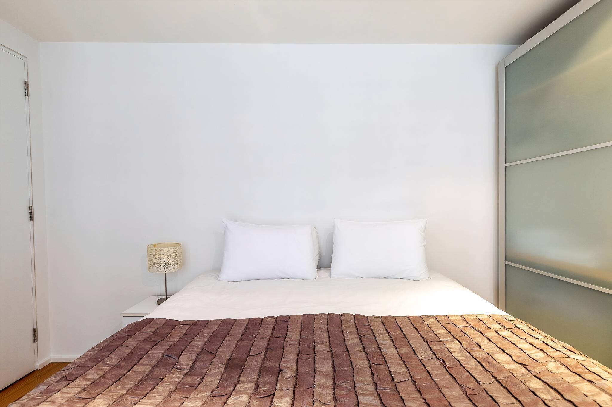 Une chambre à coucher avec une couvre-lit à motifs de briques, du linge de lit blanc et une table de chevet avec une lampe.
