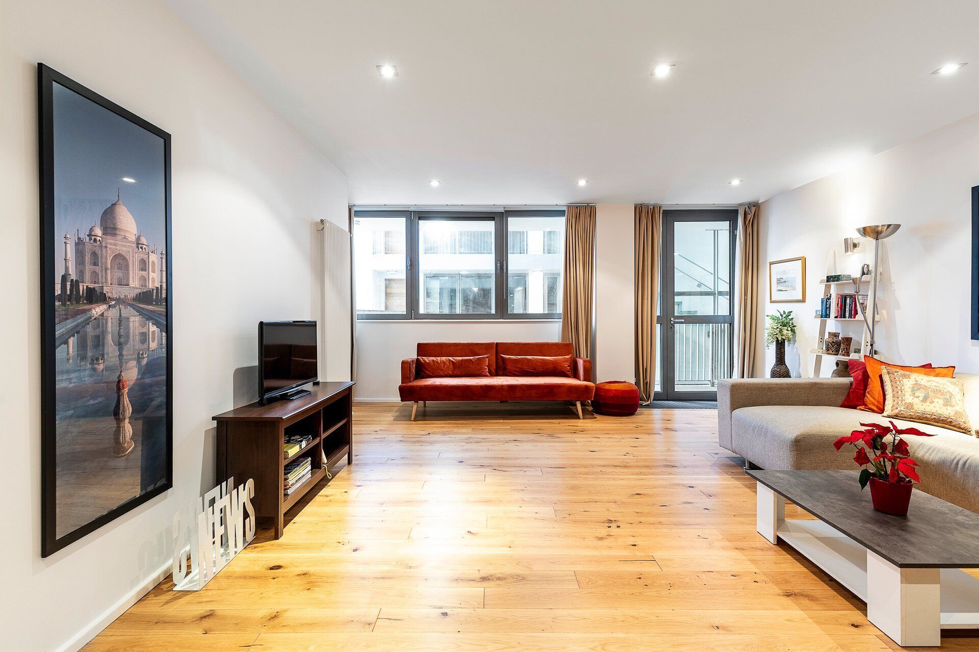A modern living room with a large window, a red sofa, a grey sofa, a wooden coffee table, and a TV on a wooden stand.