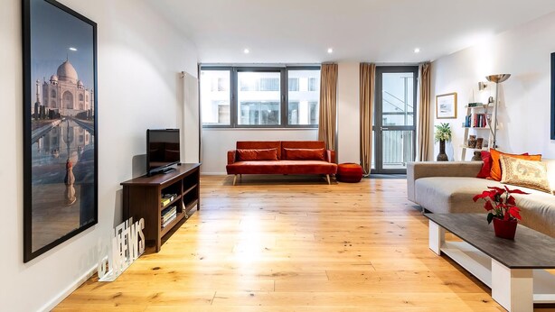 A spacious living room with a large window, a red sofa, a beige sofa, a coffee table with a plant, and a TV on a wooden stand. - The Spaceworks Stylish Flat Near Shoreditch (London)