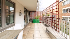 A narrow outdoor corridor with a tiled floor, a green planter, and a red fence. - The Spaceworks Stylish Flat Near Shoreditch (London)