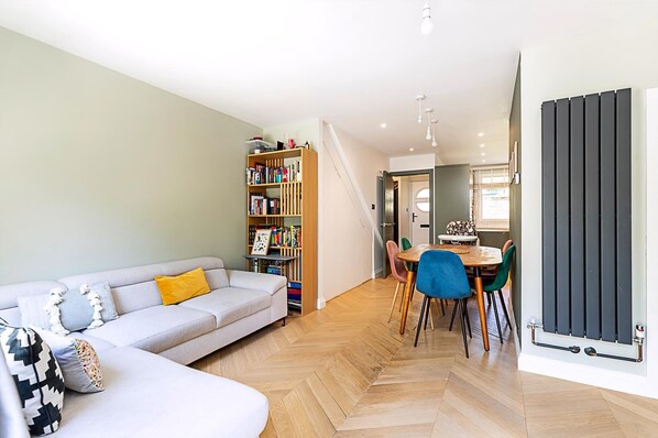 A modern living room with a sofa, a dining table with chairs, a bookshelf, and a staircase leading to another level. - Unique and Stylish 2-bed Maisonette in Islington (London)