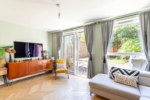A living room with a sofa, a TV, a wooden cabinet, and a chair. There is a sliding glass door leading to an outdoor area. - Unique and Stylish 2-bed Maisonette in Islington (London)