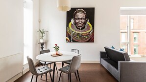 A modern living room with a round dining table, grey upholstered chairs, a grey sofa, and a large framed artwork on the wall. - Stylish Camden Flat Near Markets Tube (London)