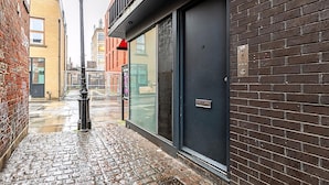 A narrow cobblestone street with a brick building, a glass door entrance, and a metal bollard. - Stylish Camden Flat Near Markets Tube (London)