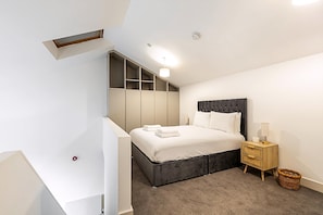 A modern bedroom with a bed, built-in storage, a bedside table, and a small window.