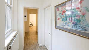 Un couloir avec un radiateur, une œuvre d’art florale encadrée accrochée au mur et une porte donnant sur une pièce.