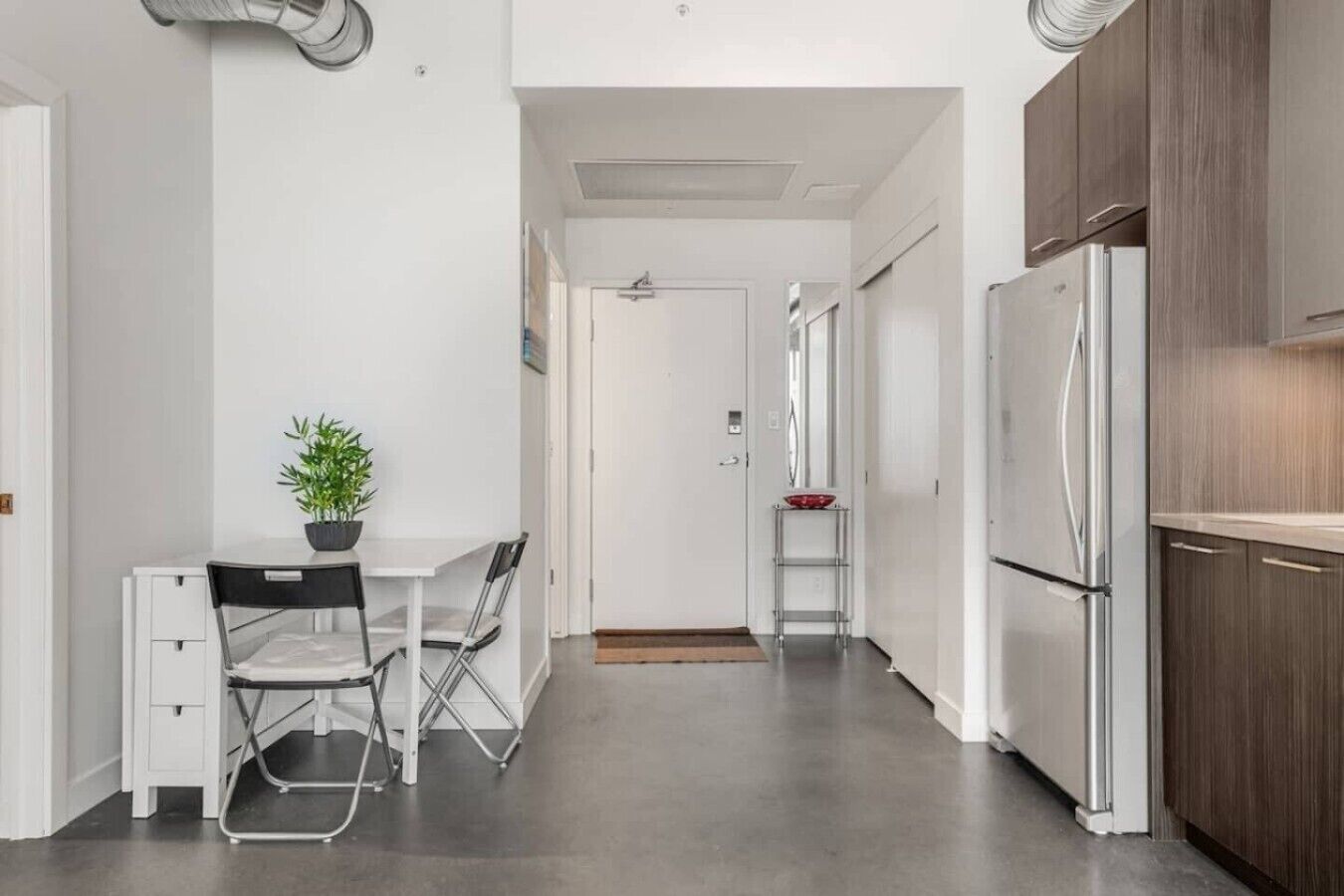 Une cuisine moderne avec des meubles blancs, un réfrigérateur en acier inoxydable, une table à manger avec des chaises et une plante en pot.