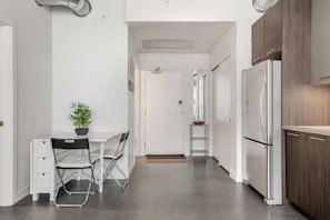 Una cocina moderna con armarios blancos, un refrigerador de acero inoxidable, una mesa de comedor con sillas y una planta en maceta.