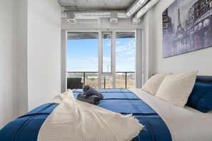 Habitación de hotel con cama, vista a través de un ventanal y un cuadro en la pared.