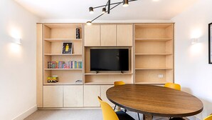 Ein modernes Wohnzimmer mit einem Holz-TV-Schrank, einem Flachbildfernseher, einem runden Holztisch und gelben Stühlen.
