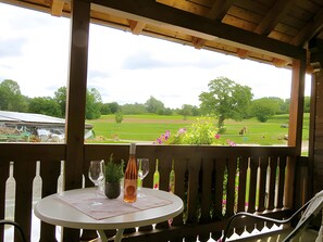 Una terraza de madera con mesa y sillas, con vistas a un campo verde y árboles.