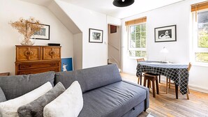 Ein modernes Wohnzimmer mit einem grauen Sofa, einer Holzkabine und einem Esstisch mit kariertem Schwarz-Weiß-Tischläufer.