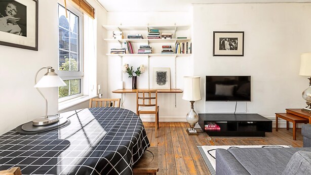 Ein modernes Wohnzimmer mit Bett, Fernseher, Bücherregal und Schreibtisch.