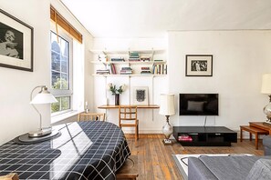 A modern living room with a bed, a TV, a bookshelf, and a desk.