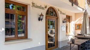 Un edificio con un letrero que dice 'Hannlins' y 'Straußi' en la fachada, una puerta de madera y una mesa con sombrilla afuera.