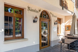 A building with a sign reading 'Hannlins' and 'Straußi' on the facade, a wooden door, and a table with an umbrella outside.