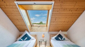 Una habitación con dos camas, un tragaluz y una mesa con lámpara.