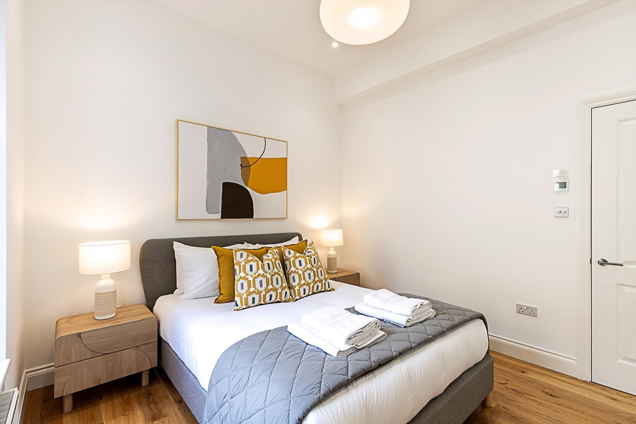 A neatly arranged bedroom with a bed, bedside lamps, a wall-mounted artwork, and a door.