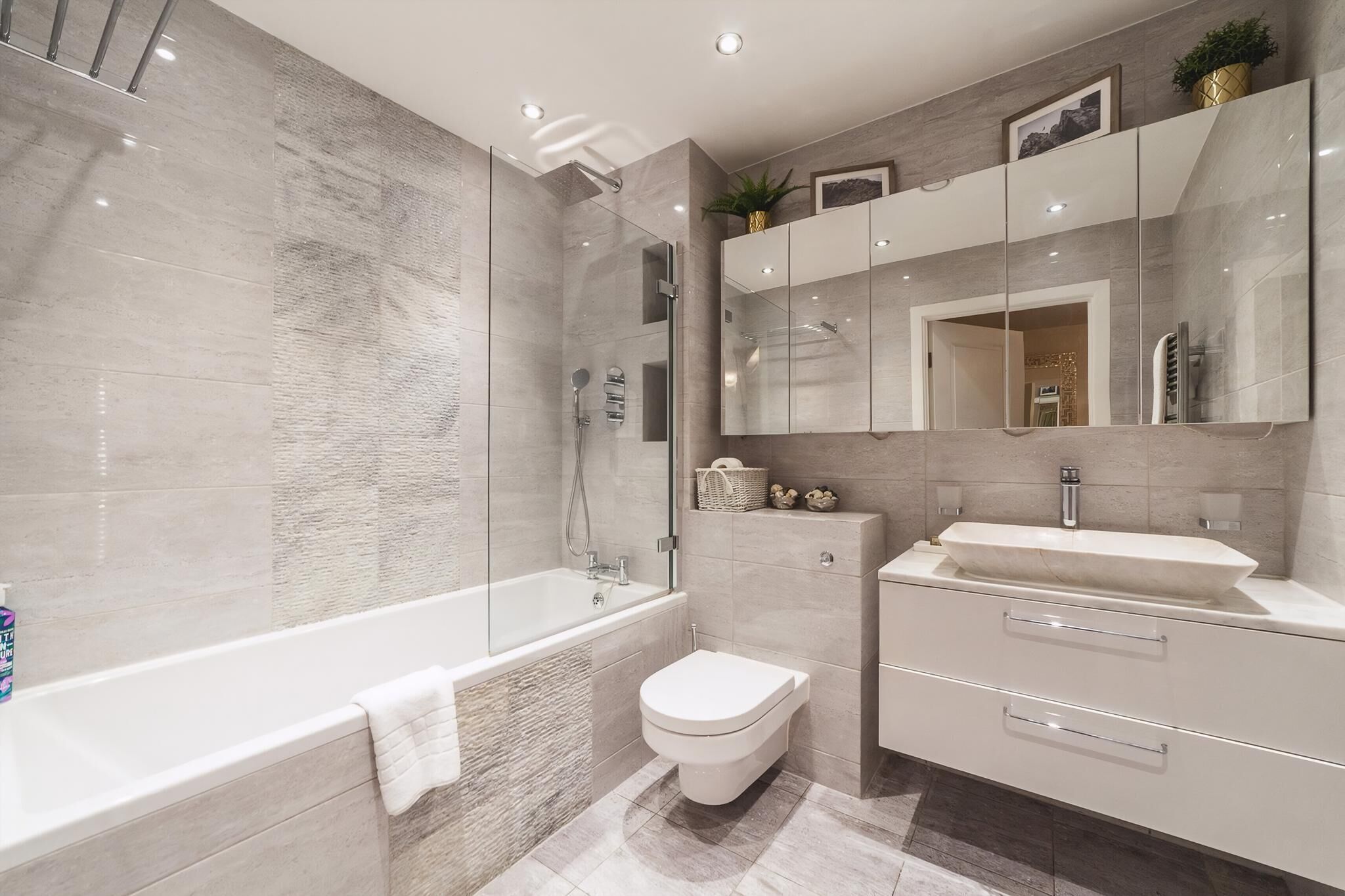 Un baño moderno con ducha de vidrio, bañera independiente, inodoro y tocador con lavabo y espejo.