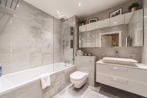 A modern bathroom with a glass-enclosed shower, a freestanding bathtub, a toilet, and a vanity with a sink and mirror. - Cosy 2-bed Poplar Flat w/ City Views (London)