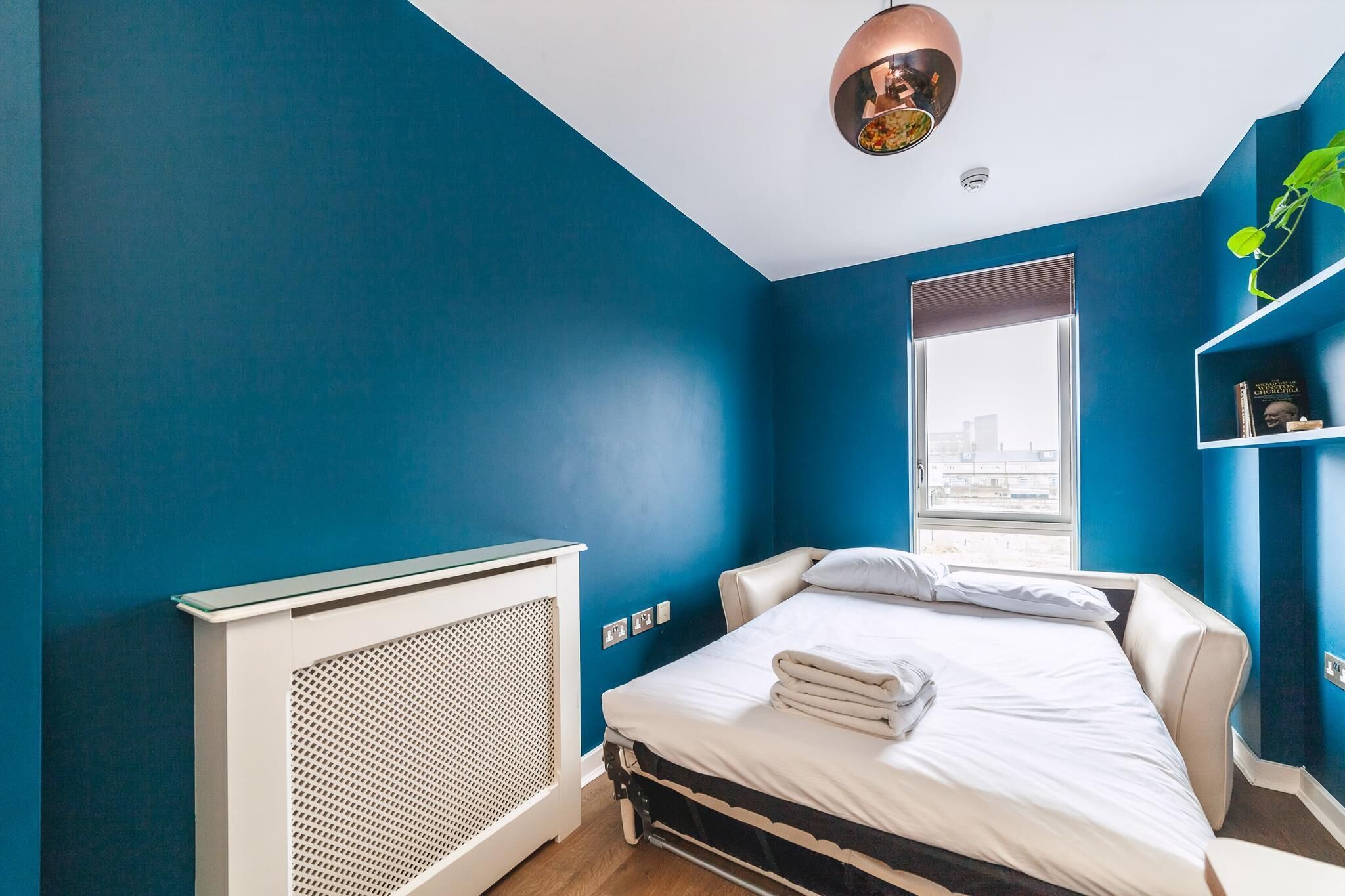 Une chambre d’hôtel moderne dotée d’un grand lit, d’un radiateur, d’une fenêtre donnant sur la ville et d’un luminaire au plafond.