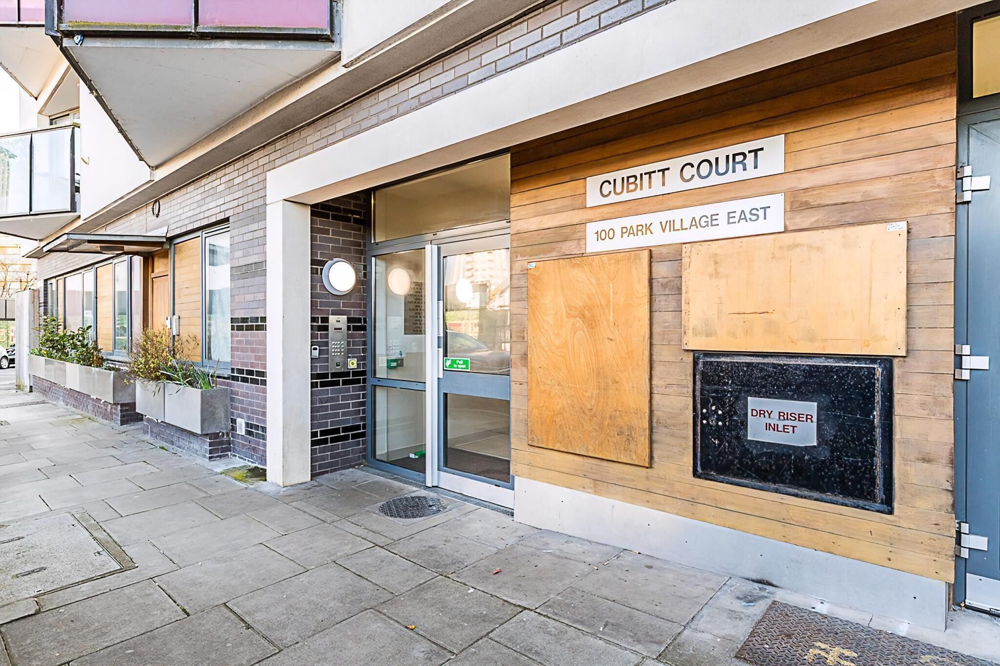 Un bâtiment moderne avec une enseigne indiquant « CUBITT COURT 100 PARK VILLAGE EAST » et une autre enseigne indiquant « ENTRÉE DE LA CONDUITE D’INCENDIE ».