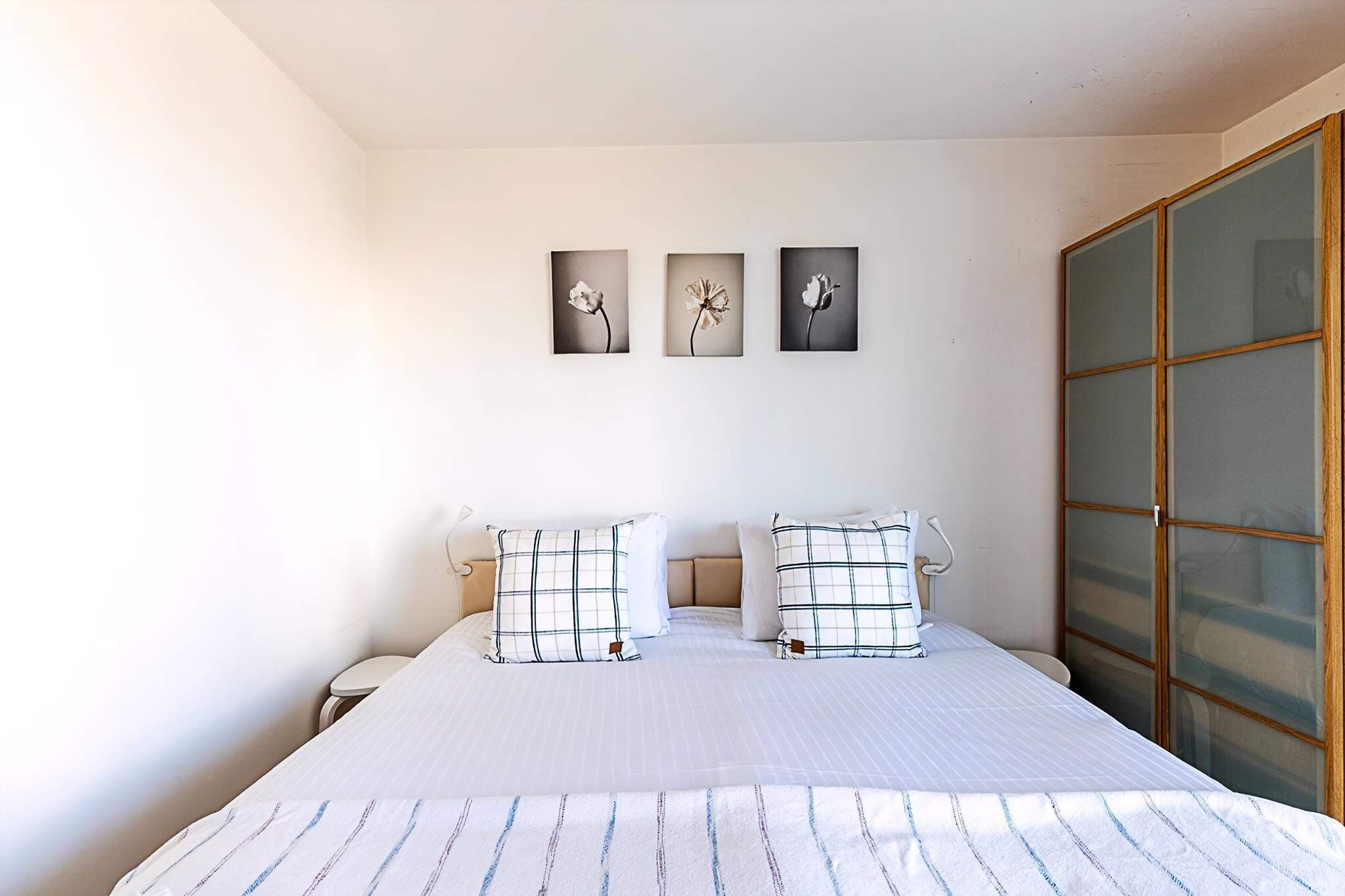 A bedroom with a bed, two bedside tables, and a large window with a view of the outside.