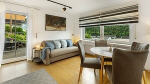 A modern living room with a sofa, dining table, chairs, and a large window with a view. - Holiday Apartment 'Schwalbennest' with Mountain View, Private Terrace and Wi-Fi (Lennestadt)