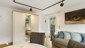 A modern living room with a sofa, a dining table, and a painting on the wall. - Holiday Apartment 'Schwalbennest' with Mountain View, Private Terrace and Wi-Fi (Lennestadt)