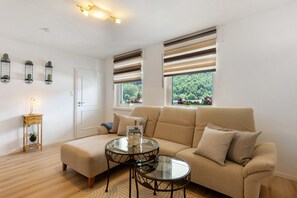 A living room with a sofa, two glass tables, a small wooden side table with a lamp, and a door.