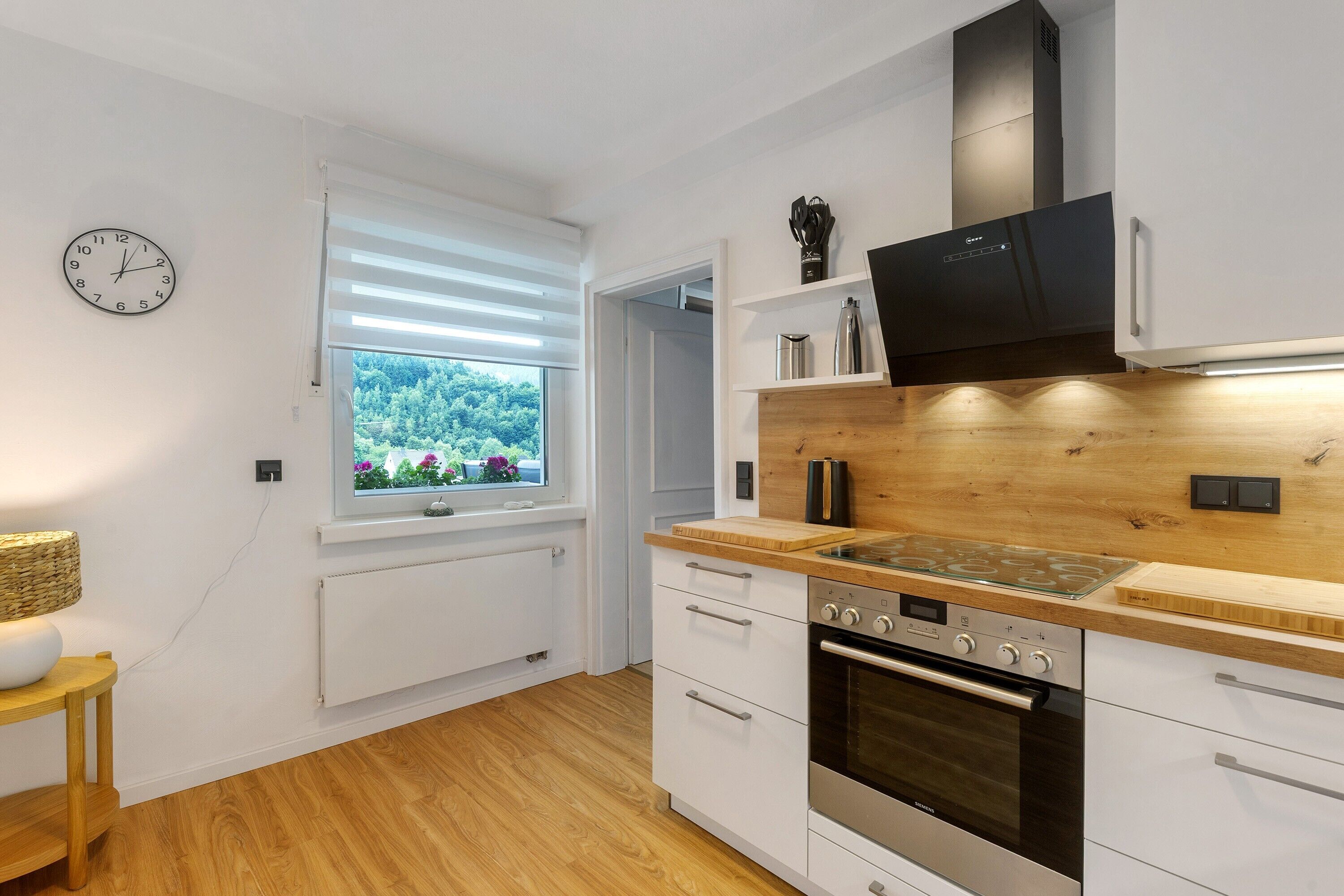 A modern kitchen with white cabinets, a built-in oven, a stove, and a window with blinds.