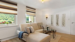 A modern living room with a sectional sofa, a glass coffee table, and a view of greenery through the window. - Holiday Apartment 'Schwalbennest' with Mountain View, Private Terrace and Wi-Fi (Lennestadt)