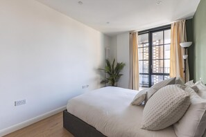 Quarto com cama, radiador, janela com cortinas e uma planta.