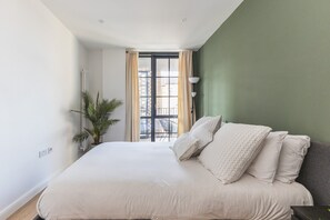A bedroom with a bed, a potted plant, a window with curtains, and a lamp. - Stylish Hackney Wick Apartment With Terrace (London)