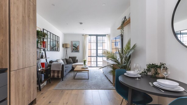 A modern living room with a sofa, coffee table, and dining area with chairs and a table set for two. - Stylish Hackney Wick Apartment With Terrace (London)