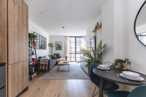 A modern living room with a sofa, coffee table, and dining area with chairs and a table set for two. - Stylish Hackney Wick Apartment With Terrace (London)