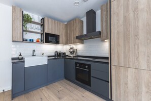 A modern kitchen with a microwave, toaster, and oven, wooden cabinets, and a white tiled backsplash. - Stylish Hackney Wick Apartment With Terrace (London)
