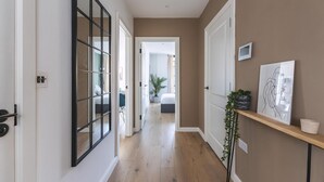 A hallway with a wooden floor, a glass door, and a shelf with a plant and artwork. - Stylish Hackney Wick Apartment With Terrace (London)