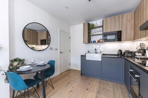 Cozinha moderna com micro-ondas, pia e armários de madeira. Possui uma área de refeições com mesa redonda e cadeiras azuis.
