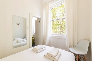 A hotel room with a bed, a chair, a mirror, and a window with a view of trees. - Elegant Knightsbridge Flat Near Harrods (London)