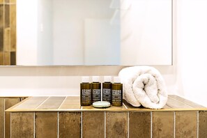 A bathroom with a tiled floor, a white towel, and three bottles of Stone Street Soaphouse products. - Elegant Knightsbridge Flat Near Harrods (London)
