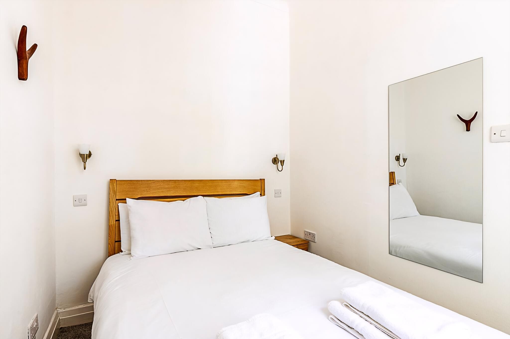 A hotel room with a wooden bed, white bedding, a wall-mounted mirror, and a small nightstand.