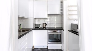 A compact kitchen with white cabinets, a black countertop, a toaster, a kettle, and an oven. - Elegant Knightsbridge Flat Near Harrods (London)