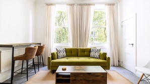 A room with a green sofa, two chairs, a wooden coffee table, and a radiator. - Elegant Knightsbridge Flat Near Harrods (London)
