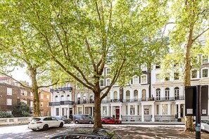 A tree-lined street with parked cars and a row of white buildings with balconies. - Elegant Knightsbridge Flat Near Harrods (London)