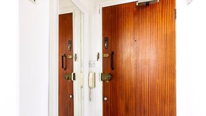 A wooden door with a brass handle and a keyhole, a white wall, and a small window. - Elegant Knightsbridge Flat Near Harrods (London)
